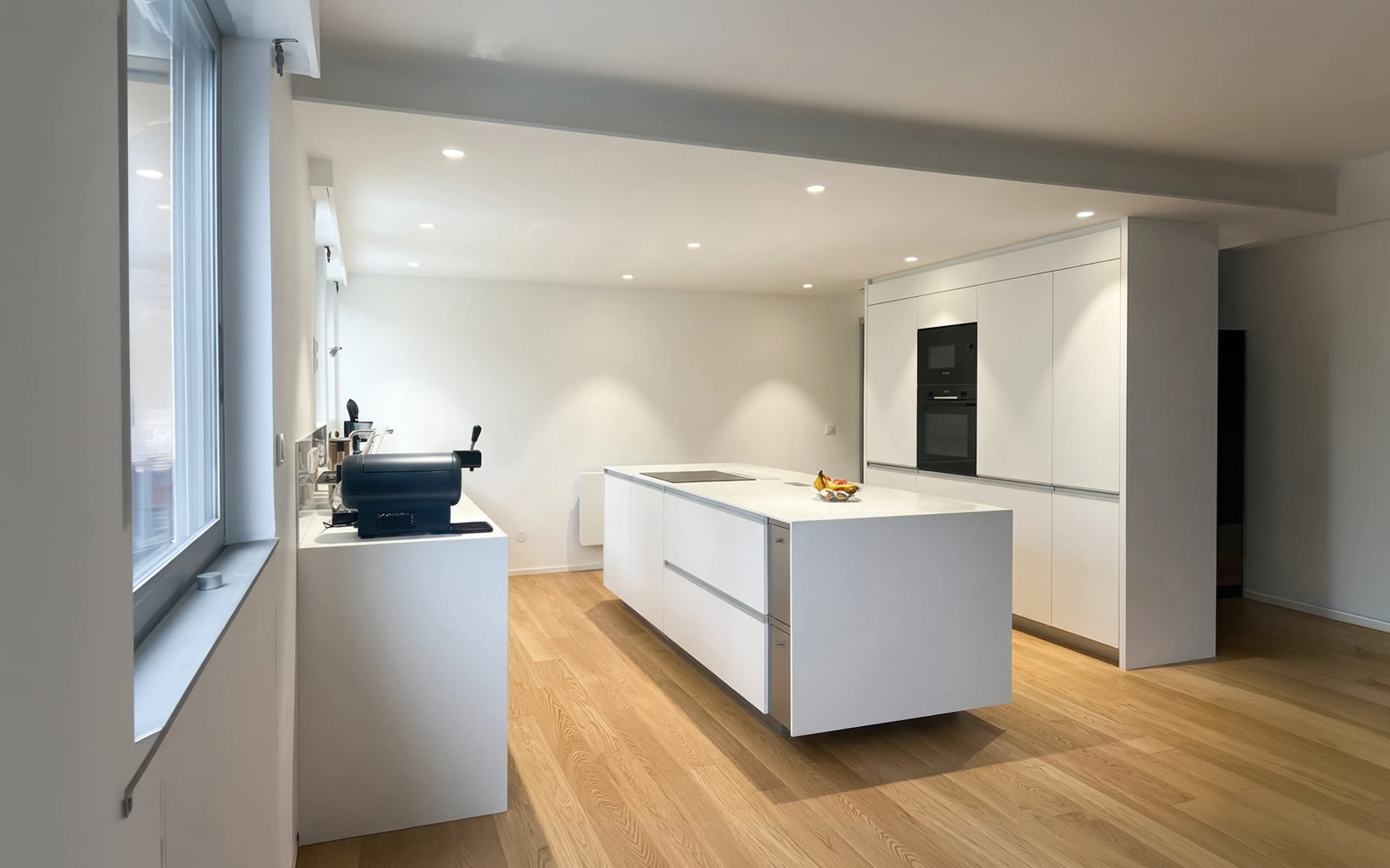 Cuisine moderne minimaliste avec îlot central blanc laqué mat, plan de travail en Corian, plaques à induction intégrées