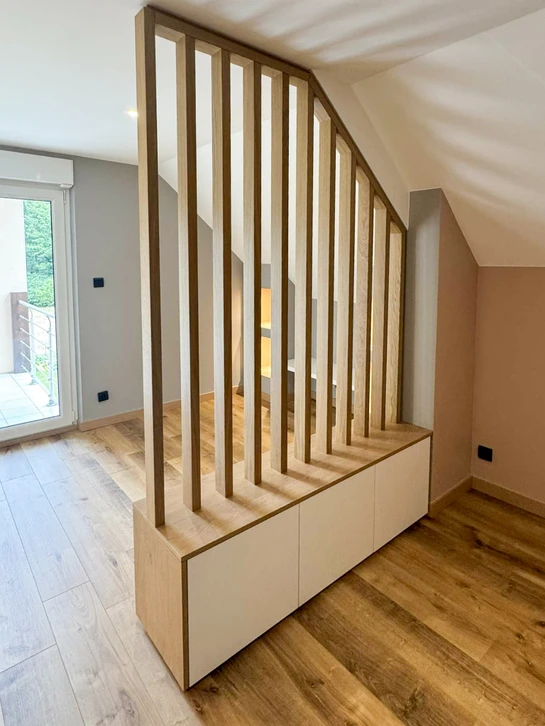 Bureau d'études moderne et épuré d'une menuiserie artisanale. Un menuisier ou technicien en tenue professionnelle travaille à un bureau en bois naturel face à un écran d'ordinateur affichant une visualisation 3D d'un meuble ou cuisine. Sur le bureau : plans techniques, documents de conception, règle, stylo. Luminosité naturelle douce, ambiance professionnelle et chaleureuse. L'image doit transmettre l'expertise technique et l'accompagnement personnalisé dans la conception des projets de mobilier sur mesure.
