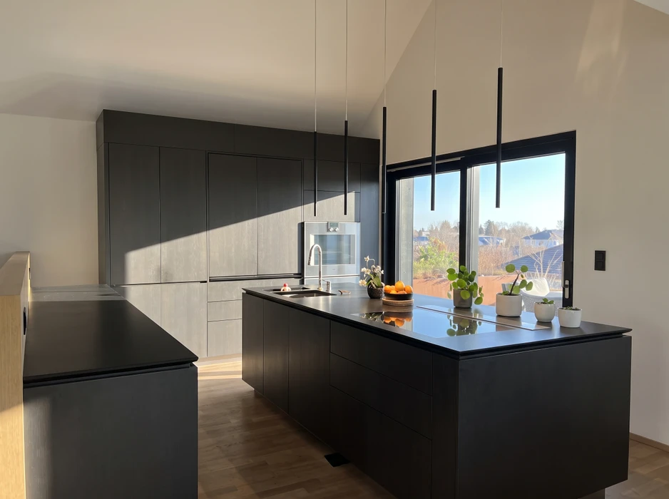 Cuisine aménagée en combles avec plan de travail vert olive en L, façades de meubles bas en stratifié imitation noyer, poignées noires