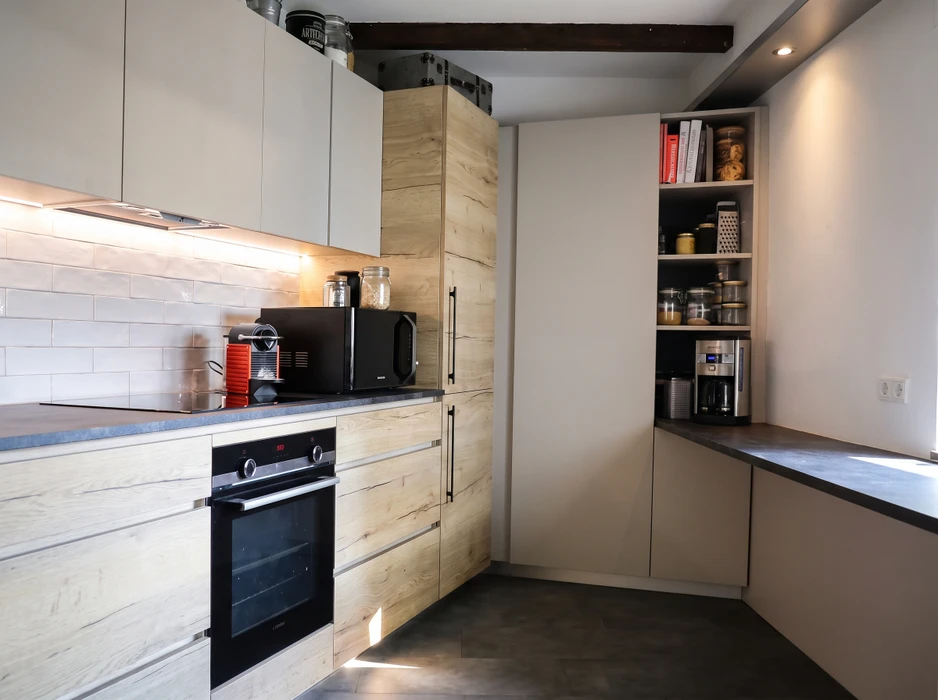 Cuisine aménagée en combles avec plan de travail vert olive en L, façades de meubles bas en stratifié imitation noyer, poignées noires